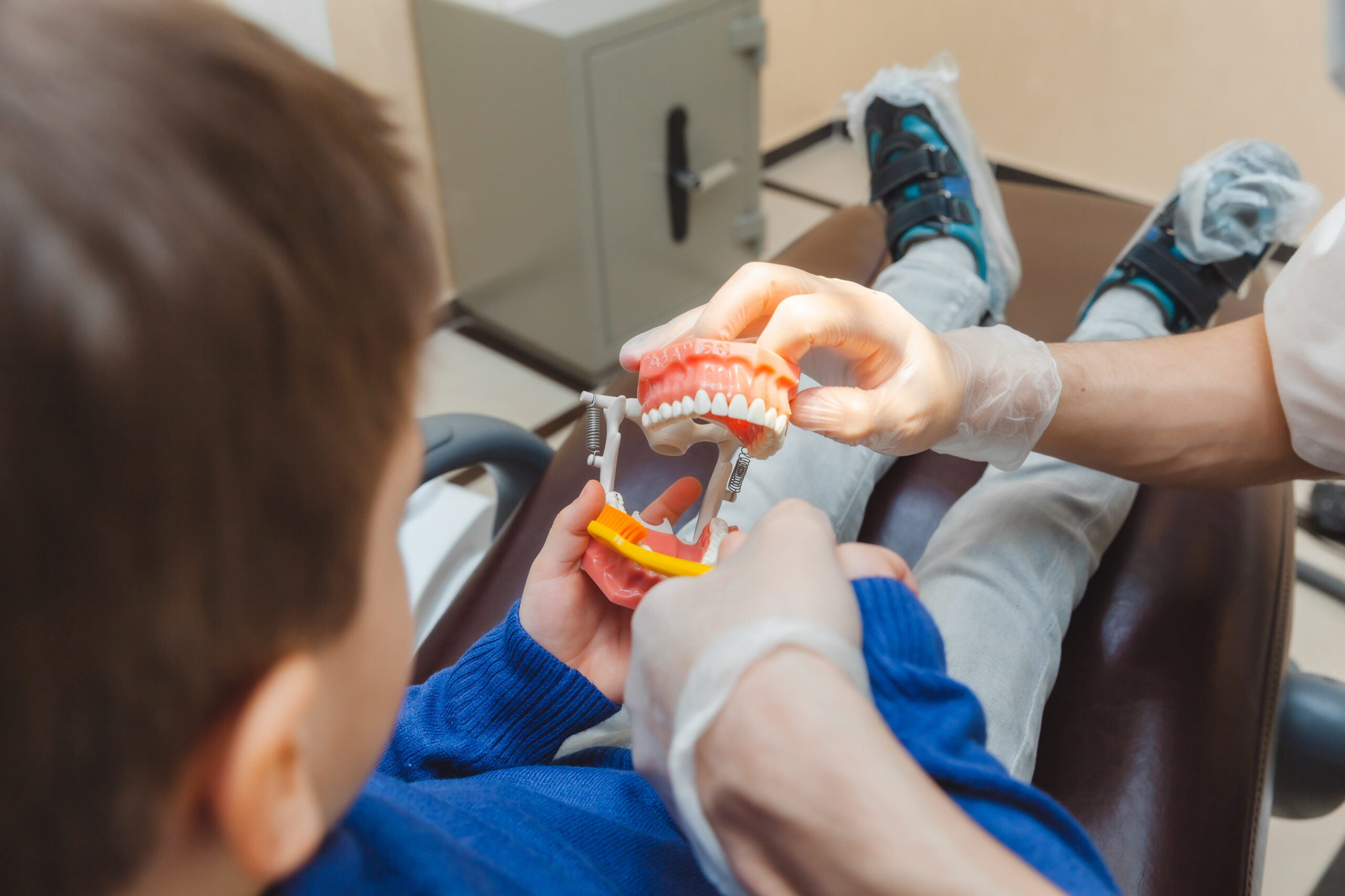 Criança aprendendo a escovar os dentes com modelo odontológico em consultório.