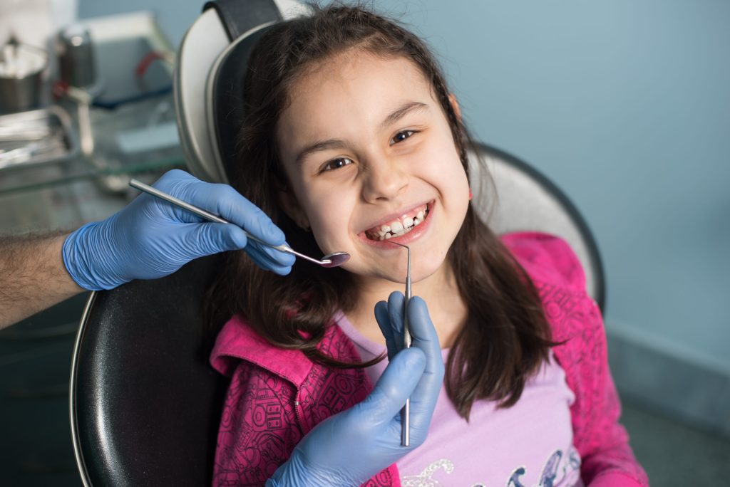 Criança em consulta com dentista infantil usando luvas azuis
