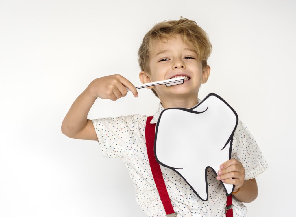 Criança sorridente escovando os dentes e segurando desenho de dente, promovendo a saúde bucal infantil como orientado na Sorridents Porto Alegre.