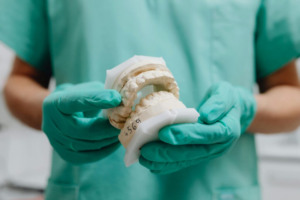 Dentista segurando molde de prótese dentária com luvas verdes em clínica odontológica em Porto Alegre.